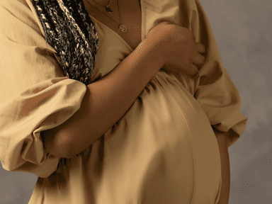 A woman in a tan dress holding her stomach.