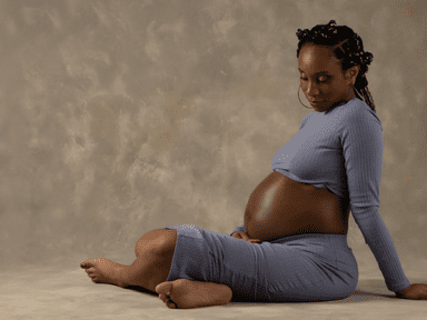 A pregnant woman sitting on the ground in her underwear.