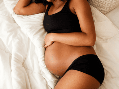 A pregnant woman laying in bed wearing black underwear.