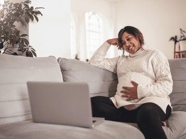A pregnant woman sitting on the couch with her laptop