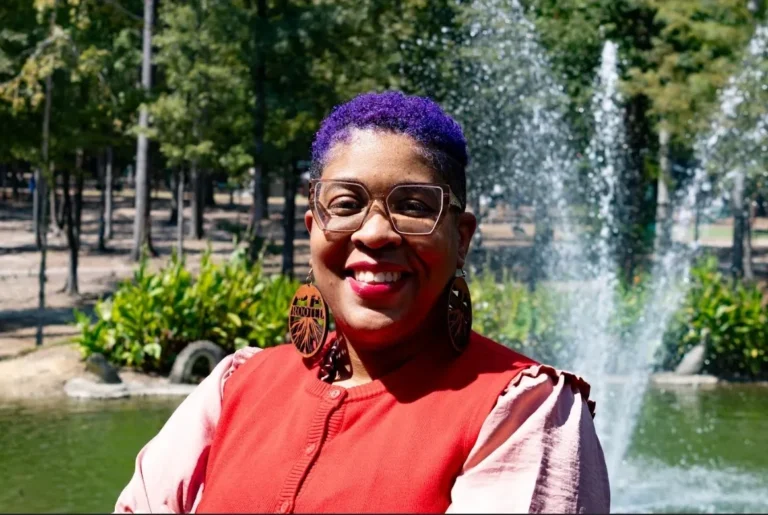 Smiling person in park with fountain backdrop.